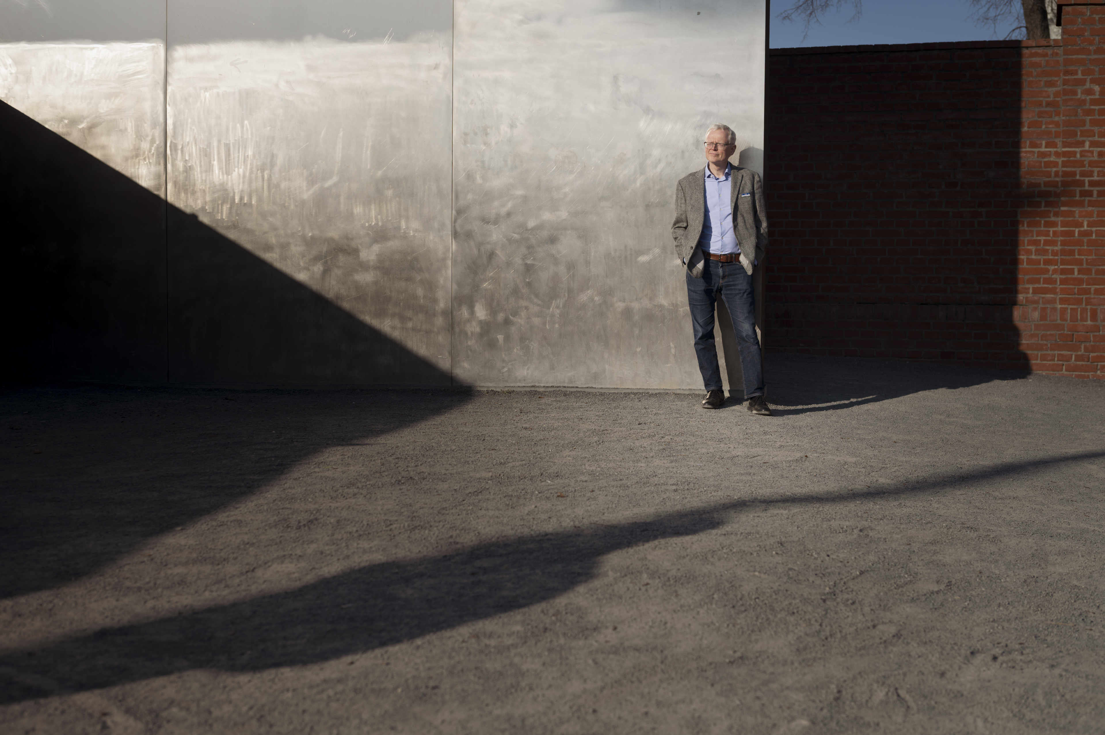 Ian Johnson stands in the sun and leans against a wall