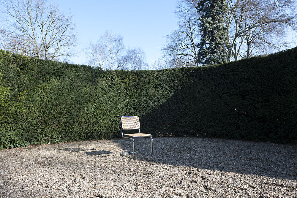 Leerer Thonet-Stuhl im Freien vor Hecke