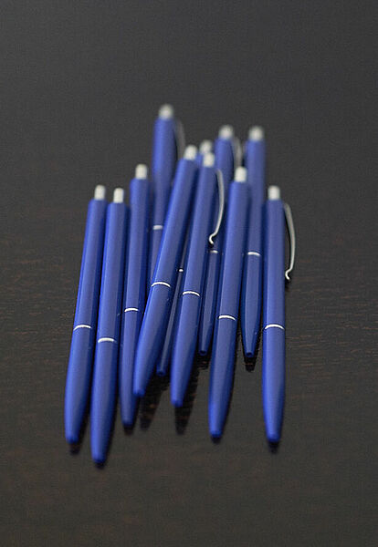 Blaue Kugelschreiber auf dunkelbraunem Tisch.